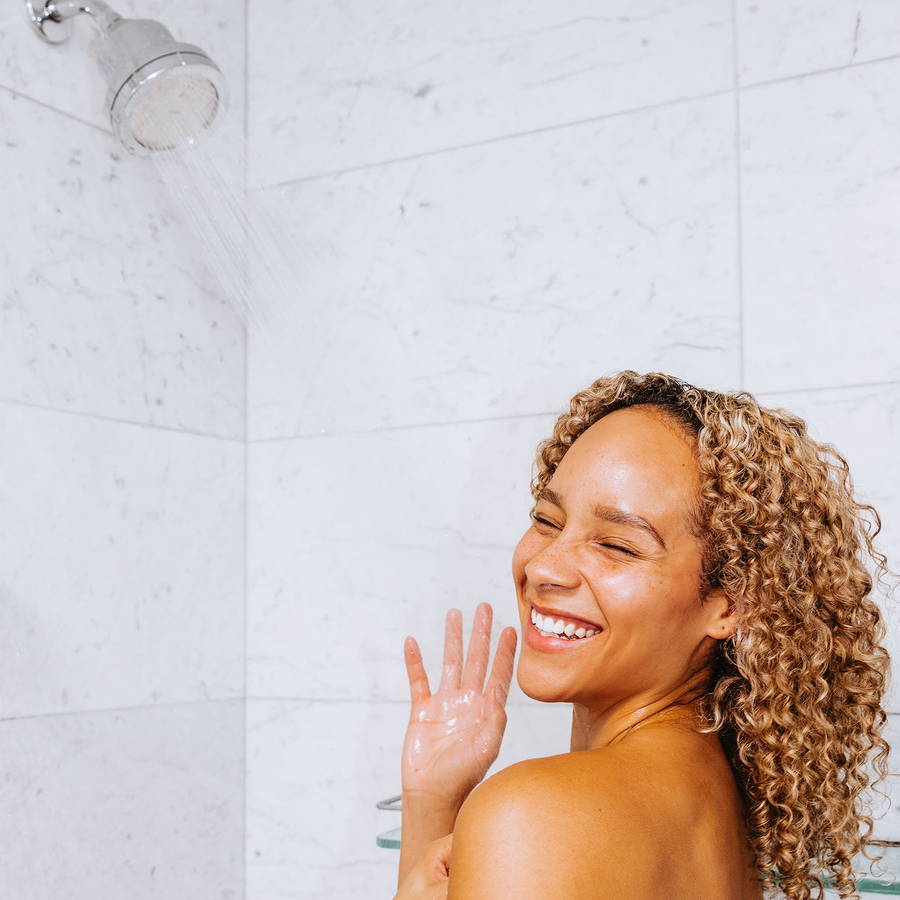 Person smiling while taking a shower under a chrome showerhead.