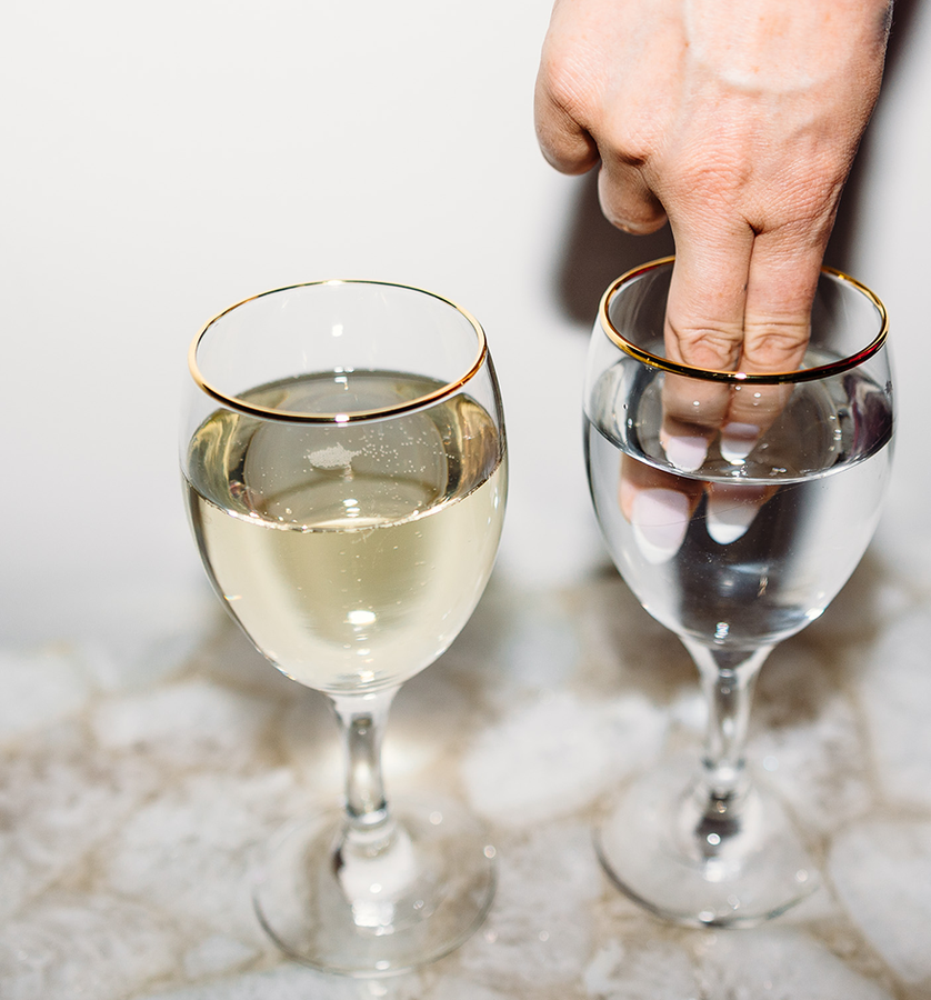Hand dipping fingers into a wine glass next to another filled glass.