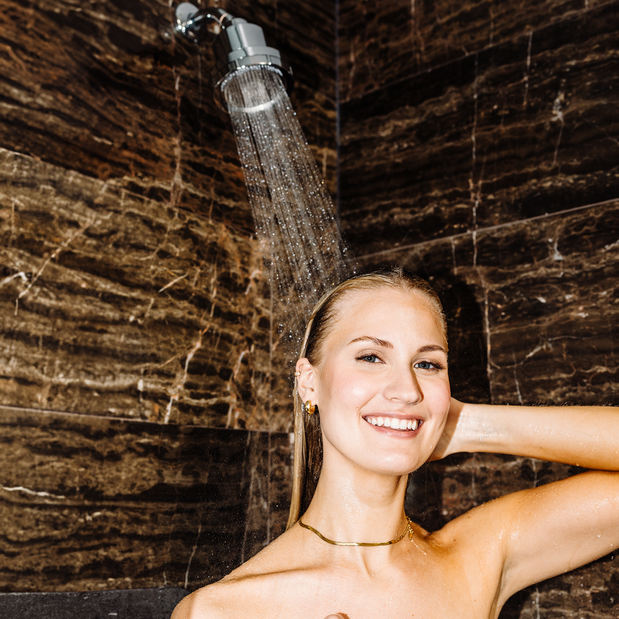 Person enjoying a shower with a smiling expression, in a brown-tiled bathroom.